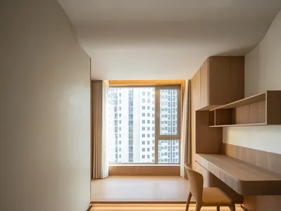 A minimalist apartment study room with a wood desk, chair, and shelving.
