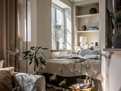 A minimalist bedroom featuring neutral-toned fabrics, light-colored wood, and plants