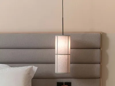 A modern minimalist bedroom featuring a textured headboard with a hanging pendant light above a side table.