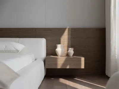 Minimalist bedroom featuring a white bed with fluffy pillows and a floating wooden nightstand with two decorative vases.