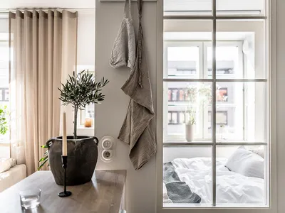 A minimalist bedroom featuring neutral-toned furniture, textiles, and decor, with a window providing natural light.