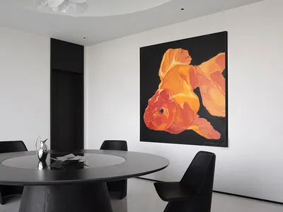 A minimalist design featuring black and white elements, a round table, black chairs, and a large goldfish artwork on the wall