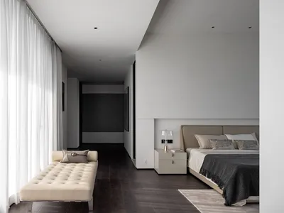 Modern bedroom with neutral decor, featuring a minimalist bed and a beige lounge chair.
