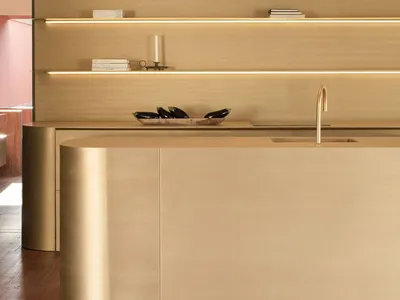 A view of a modern metallic kitchen counter with a brass faucet and a wooden backsplash.
