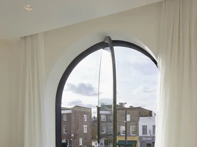 A modern bedroom features a glass window overlooking a residential area.