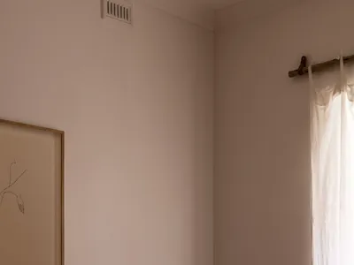 A minimalist bedroom with light brown fabric bedding and a window with light filtering through the curtain.