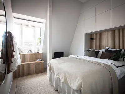A minimalist bedroom featuring a wooden headboard, white linens, and a window seat.