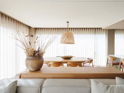 Minimalist-designed living and dining area with wooden tables and chairs, and a large vase with dried flowers.