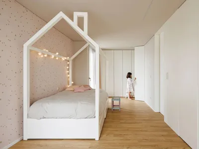 Modern children's bedroom with a house-shaped frame bed, wood flooring, and soft textiles.