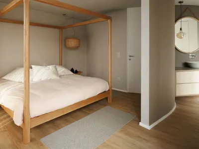Minimalist bedroom with a wooden bed frame, rounded corner column, and grey flooring