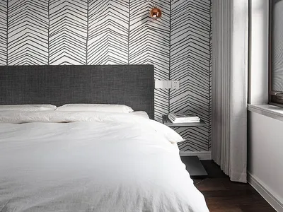 Modern, minimalist bedroom with a grey fabric headboard, white bedding, and geometric wallpaper.