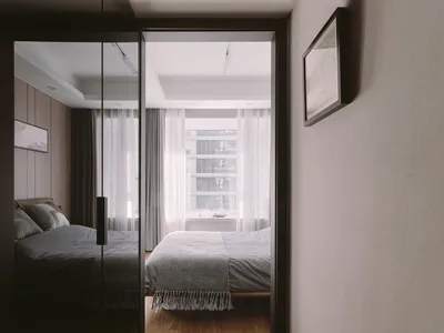 A minimalist bedroom featuring a bed with white curtains and a grey bedspread, set against a grey wall and hardwood floor.