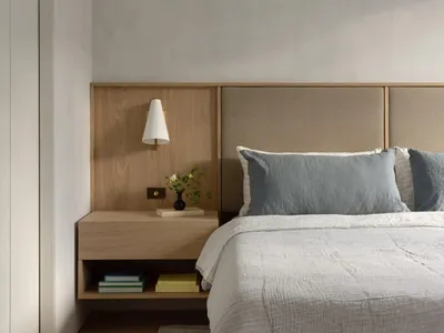 A minimalist bedroom featuring a wooden headboard and fabric blanket on a bed with books and a plant on a floating nightstand
