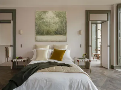 A serene, minimalist bedroom featuring a single bed adorned with white and mustard-colored pillows, a green blanket, and a pa