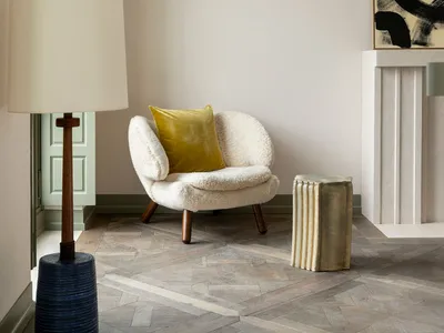 A cozy living room with a white armchair and mustard yellow pillow, featuring a wooden floor and a door in pastel green.