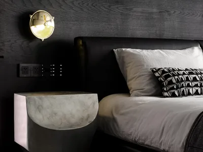 A modern bedroom featuring a concrete nightstand, a black leather bed, and a metal bedside lamp.