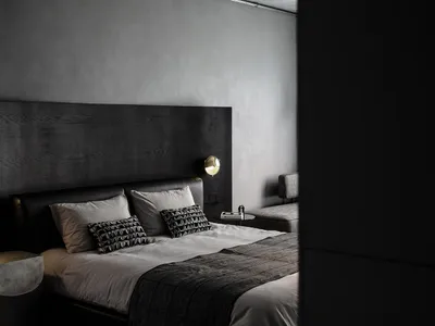 A minimalist bedroom with a dark wood headboard and light bedding, featuring modern sconce lighting and a sleek, low-profile