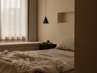 A minimalist bedroom with neutral-toned fabrics, featuring a bed, window with curtains, and a hanging lamp.