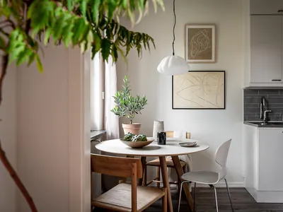 A minimalist kitchen with white furniture, a round table, and a white pendant light hanging above it.