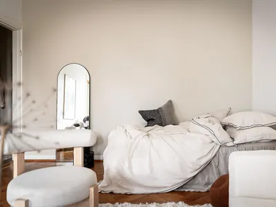 A minimalistic bedroom with a bed covered in white linen, wooden furniture, and a large mirror on the wall.