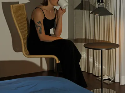 A minimalist bedroom with a black chair, bed, and hanging lamp.