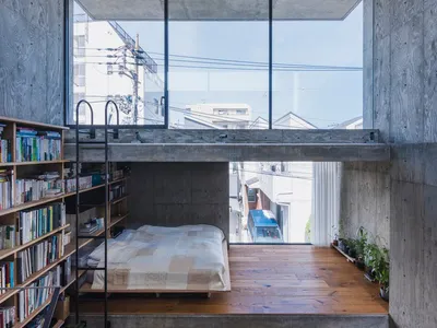 A minimalist bedroom featuring a concrete floor and wall, with a bed on a raised platform and a bookshelf.