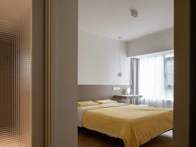 Modern minimalist bedroom with a yellow blanket and a bed, featuring clean lines and a white ceiling light.