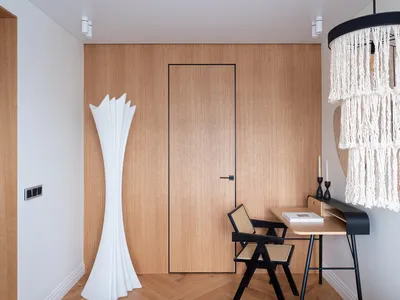 A modern home office features a wooden wall with a closed door, a sleek desk, and a minimalist white floor lamp.