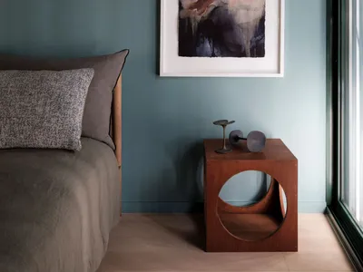 Modern bedroom featuring a wooden nightstand with abstract art and a cozy bed.