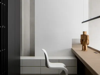 A minimalist home office with a sleek, white chair on a concrete floor, and a wooden desk with a modern sculpture next to it.