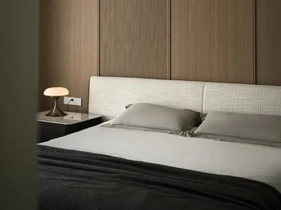 A minimalist bedroom with a white fabric headboard, textured paneling, and a wooden bedside table.