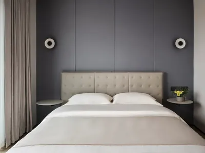 A neatly made bed with white sheets and pillows against a grey wall, featuring a simple headboard and side tables with a vase