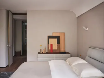 A minimalist bedroom featuring a modern wooden dresser with decorative items and a comfortable bed.