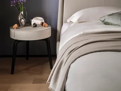 A minimalist bedroom featuring a bed with a beige leather headboard and fabric bedding.