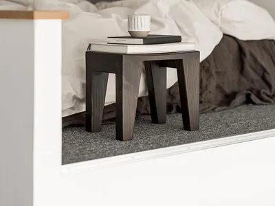 A minimalist bedroom featuring a wooden bedside table with books and a mug on top.