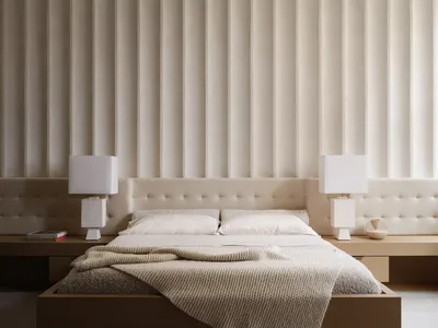 Minimalist bedroom with a white fabric bed and light-colored walls.