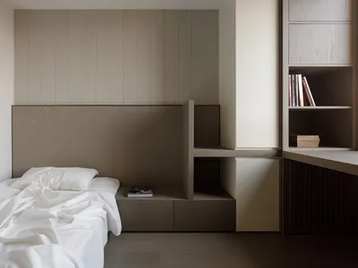 Minimalist bedroom with wooden furniture and white bedding, featuring integrated shelving and storage systems.