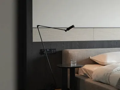 Minimalist bedroom featuring a black floor lamp and a bedside table with a glass of water.