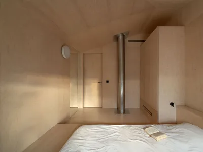 A bedroom with wooden walls and a white bedspread, featuring a minimalist design.