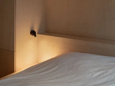 A minimalist bedroom with illuminated wood paneling and lit shelf