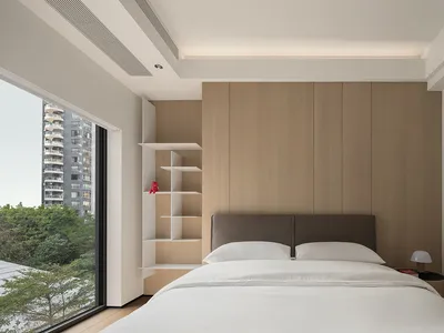 A minimalist bedroom featuring wood-paneled walls, a white bed with light-colored bedding, and a modern, open shelving unit.