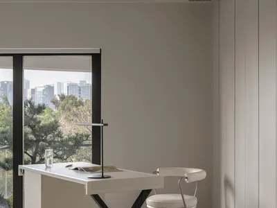 Modern home office space with sleek, minimalist desk, chair, and floor-to-ceiling windows overlooking a cityscape.