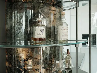 Glass shelves and bottles on a curved bar counter with a marble background.