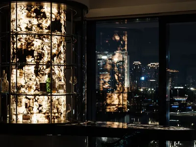 A modern bar counter featuring glass shelves and lighting, with a view of a cityscape at night.