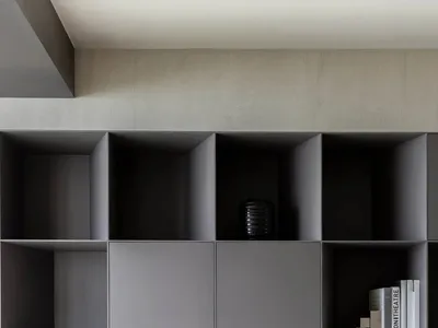 A minimalistic home office with concrete grey shelves, a red mesh office chair, a black desk lamp, and some books.
