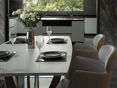 A modern kitchen with a white marble countertop and floor, featuring sleek cabinets and a large window with a view of green t