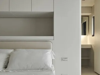 Modern minimalist bedroom featuring a neutral color palette and a neatly arranged bed with a headboard.