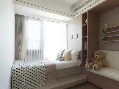 A modern neutral-toned bedroom featuring a bed with a polka-dotted blanket, a teddy bear, and a shelf with decorative items.