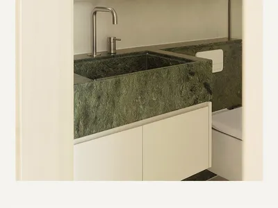 A minimalist bathroom featuring a green marble counter and white cabinets and walls, with a large mirror above the sink.