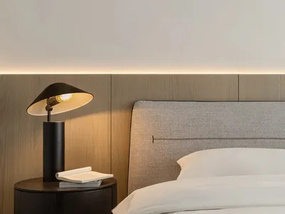 A minimalist bedroom featuring a grey upholstered headboard and white bedding.
